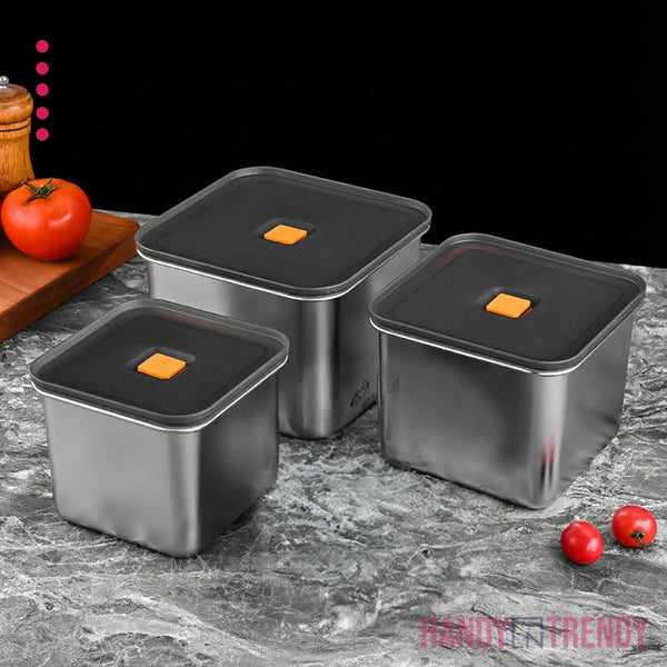 Three stainless steel containers with black lids on a gray surface, surrounded by tomatoes and a pepper.
